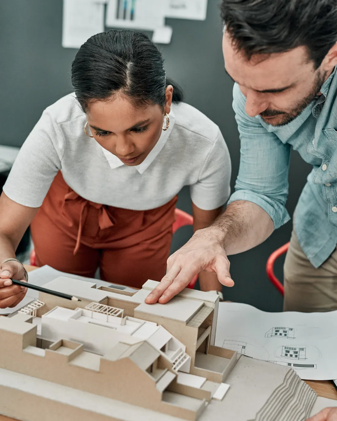 Dois arquitetos do ateliê debruçados sobre a maqueta, com os desenhos abertos ao lado.