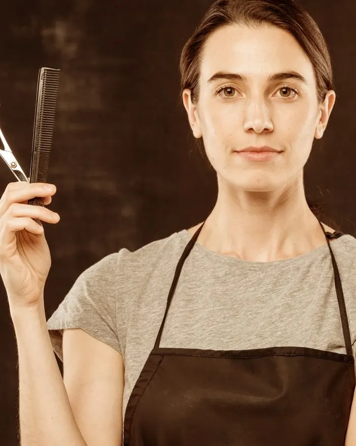 Márcia, barbeira, com tesoura e pente na mão, de avental preto.