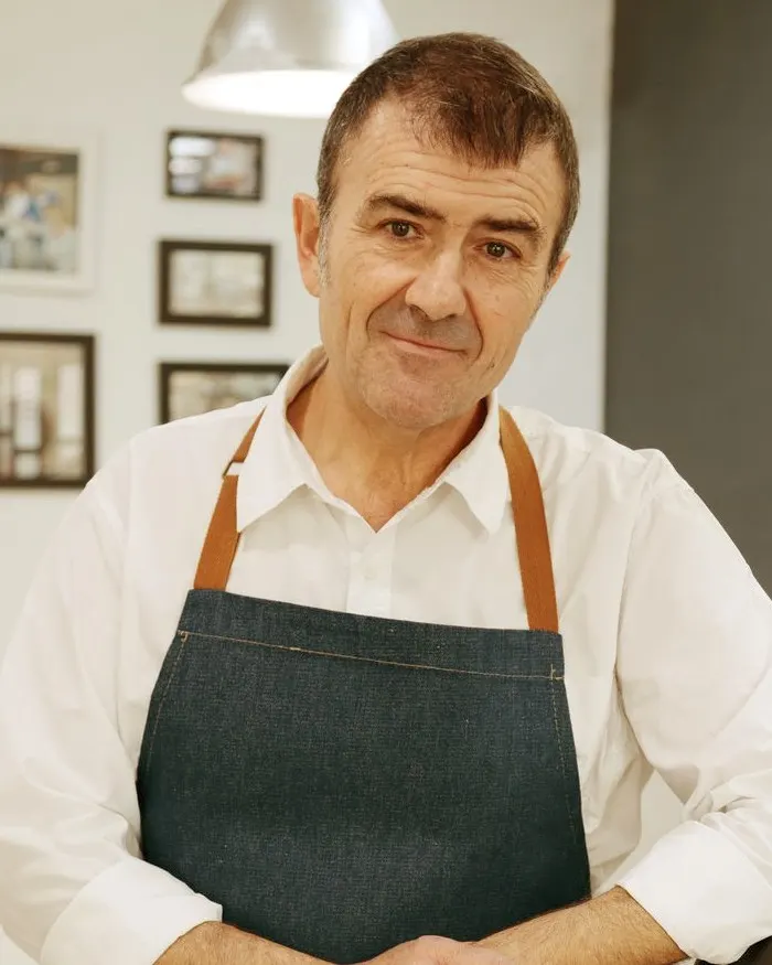 Zé Rocha, barbeiro, de avental de ganga encostado à cadeira da sua barbearia.